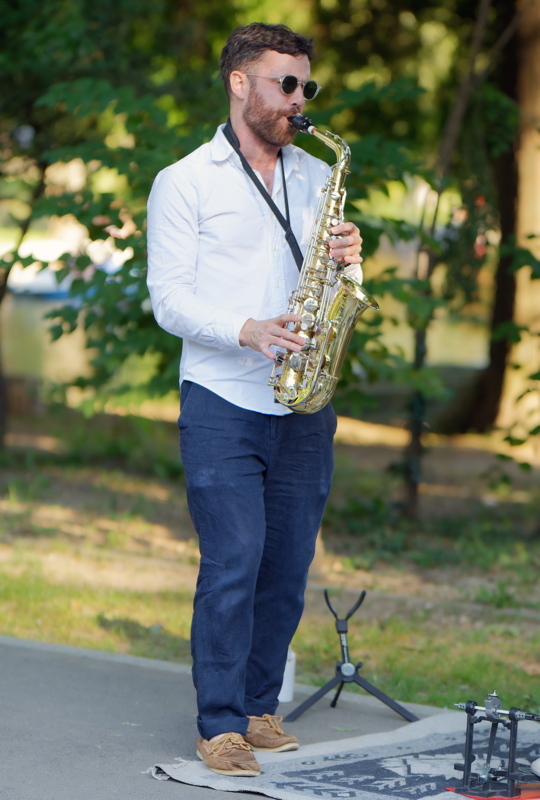 16 - A street musician playing an alto saxophone outdoors during a sunny day